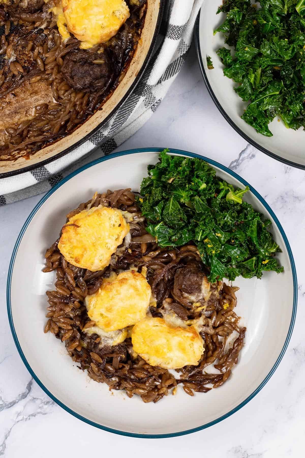 A bowl of french onion meatballs with orzo, with sautéed kale with chilli and lemon on the side.