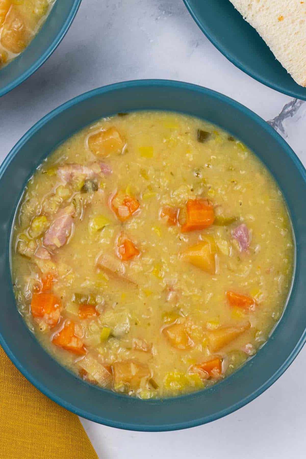 Two portions of lentil soup in teal bowls with sliced bread on the side.