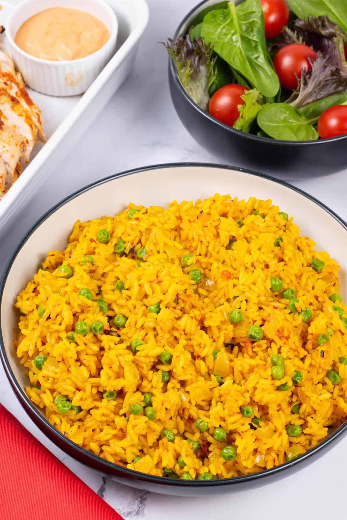 Nando's spicy rice in a black and cream serving bowl with a bowl of salad leaves and tomatoes in the background.