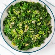 Petit pois with kale and onions in a large teal and cream serving bowl.