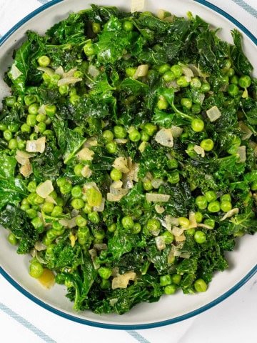 Petit pois with kale and onions in a large teal and cream serving bowl.