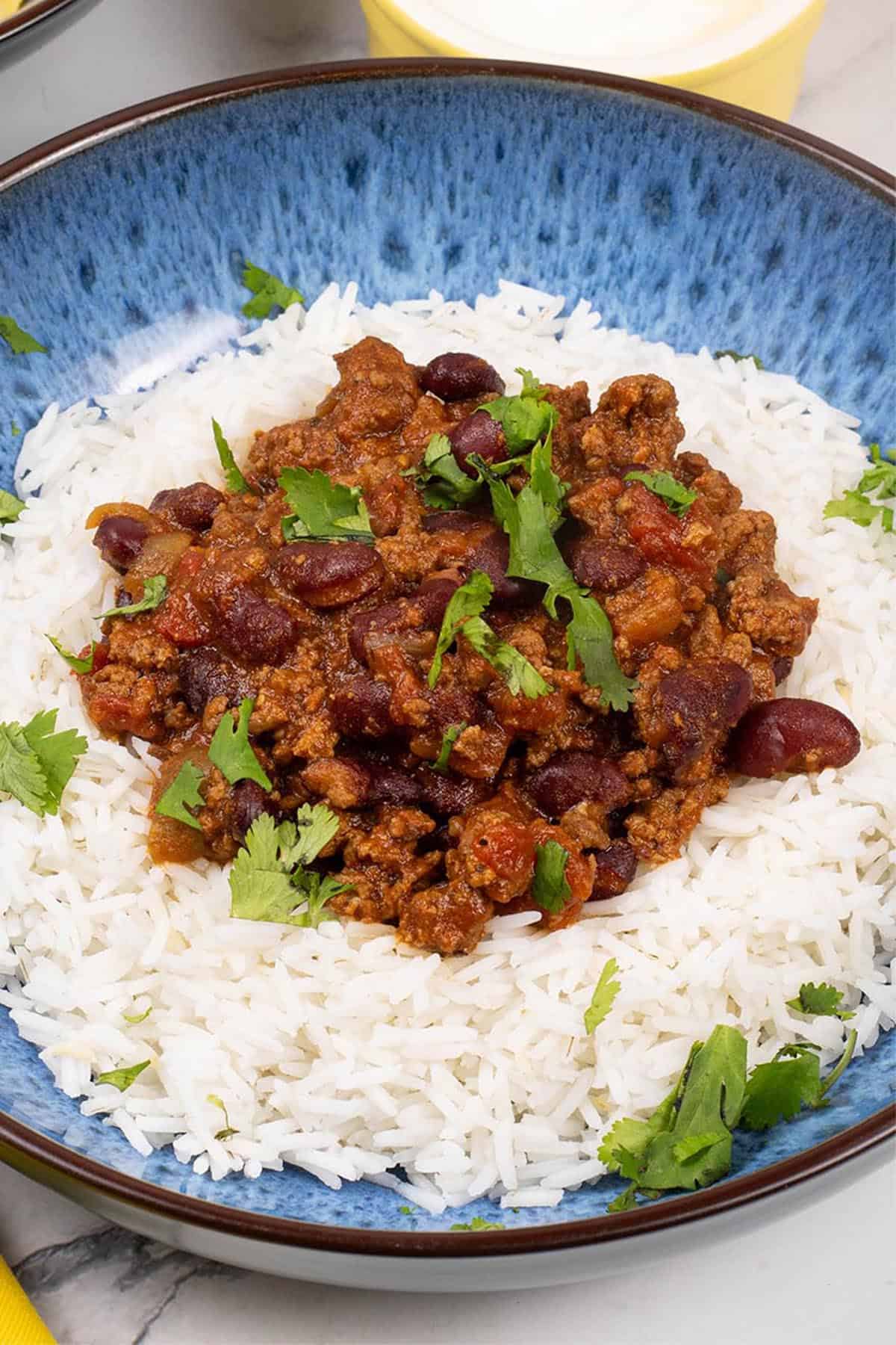 A portion of slow cooker chilli con carne on a bed of rice in a blue patterned bowl.