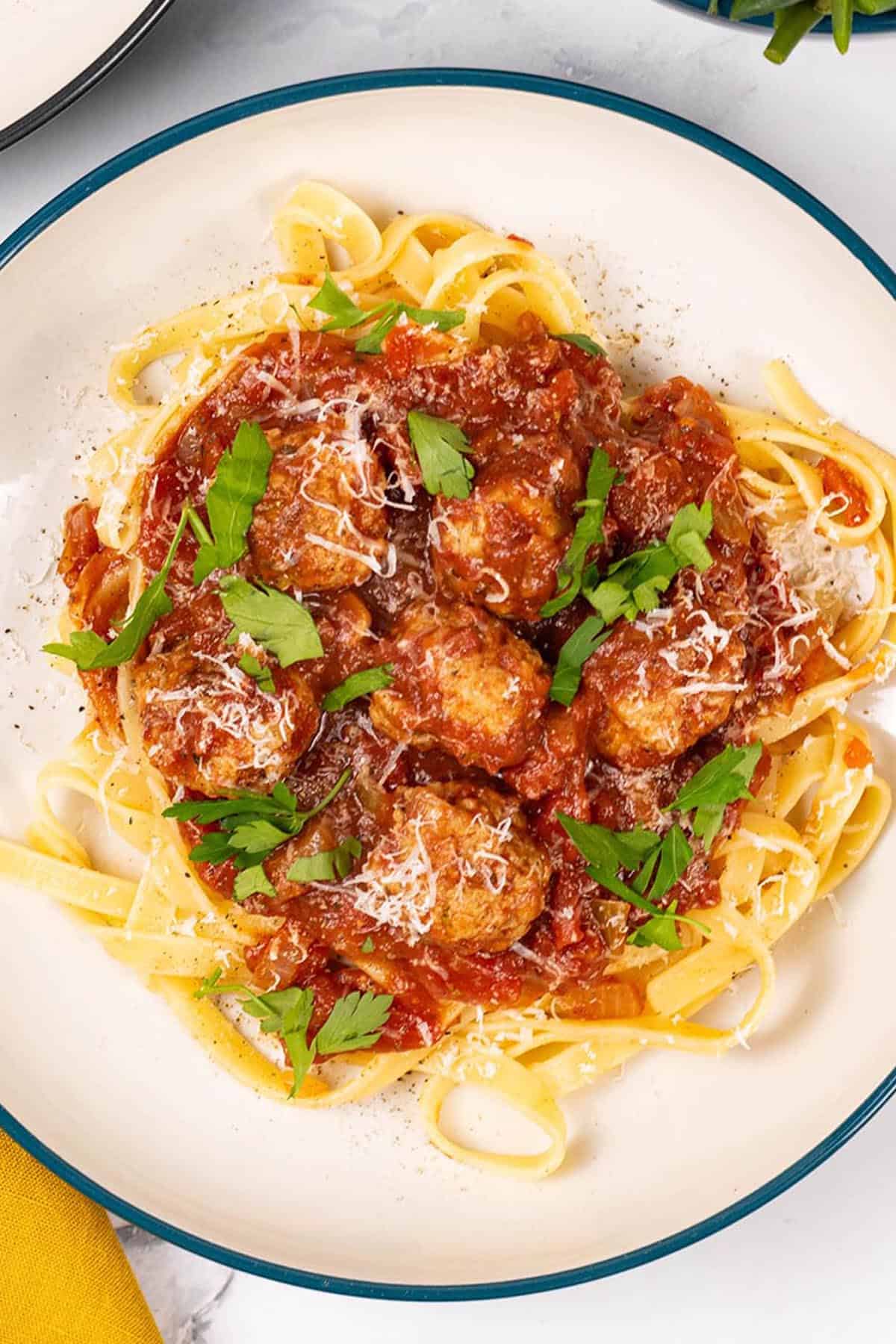 A portion of spicy sausage meatball pasta in a green and cream pasta bowl.