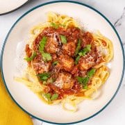 A portion of spicy sausage meatball pasta in a green and cream pasta bowl.