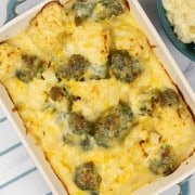 Cauliflower and broccoli cheese in a rectangle Staub oven dish with a bowl of mashed potatoes on the side.