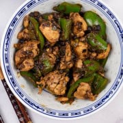 Chicken with green peppers and black bean sauce in a blue and white oriental bowl, with chopsticks on the side.