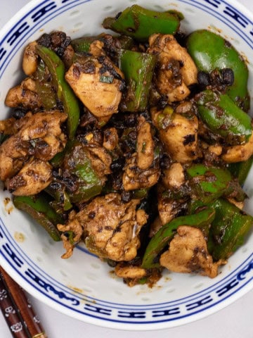 Chicken with green peppers and black bean sauce in a blue and white oriental bowl, with chopsticks on the side.