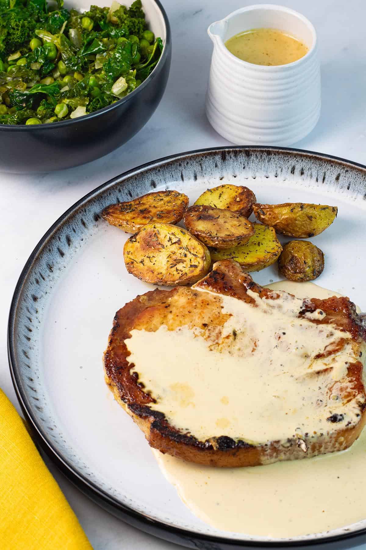 Creamy peppercorn sauce poured over a pan fried pork chop on a white and black patterned dinner plate.