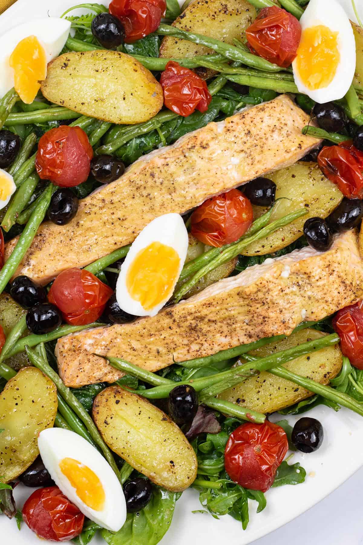 Close up of easy salmon nicoise traybake on a white serving platter.