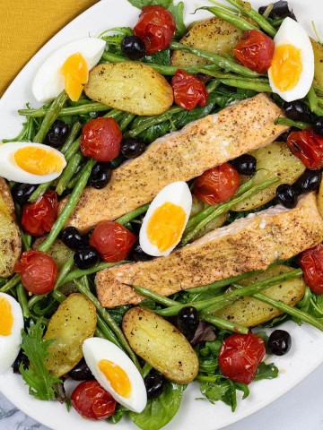 Easy salmon nicoise traybake on a white serving platter with a mustard napkin on the side.