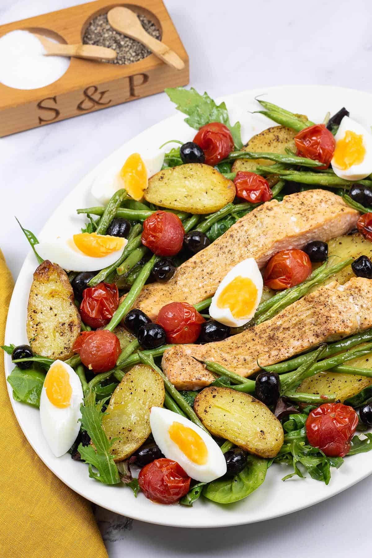 Easy salmon nicoise traybake on a white serving platter with a mustard napkin on the side.