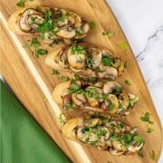 Two portions of garlic mushroom bruschetta on a board with a green napkin on the side.