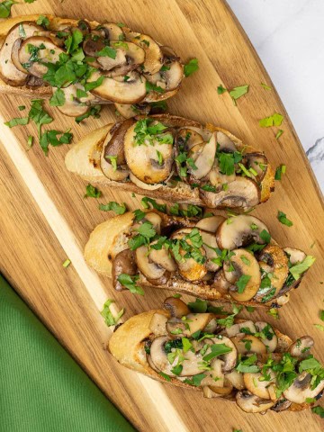 Two portions of garlic mushroom bruschetta on a board with a green napkin on the side.