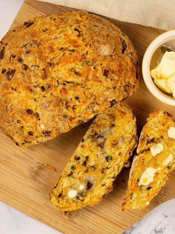 Leek and red leicester soda bread on a board with a couple of slices cut, and a small dish of butter on the side.