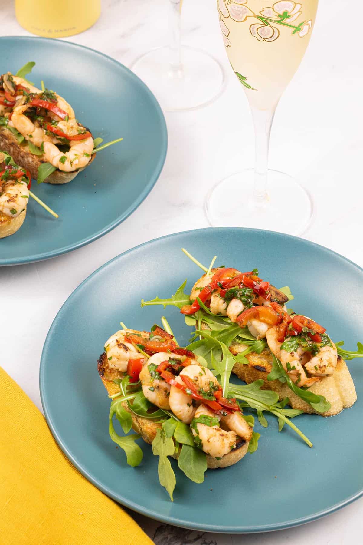 2 portions of lemony prawn bruschetta on teal side plates with 2 flutes of cava on the side.