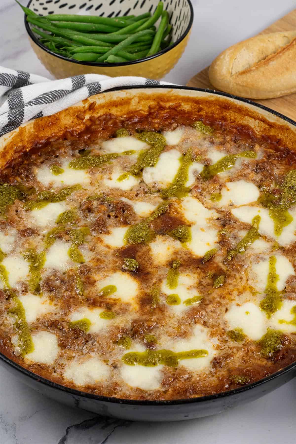 Risotto bolognese in a large shallow round casserole dish with a bowl of green beans and a crusty bread on the side.