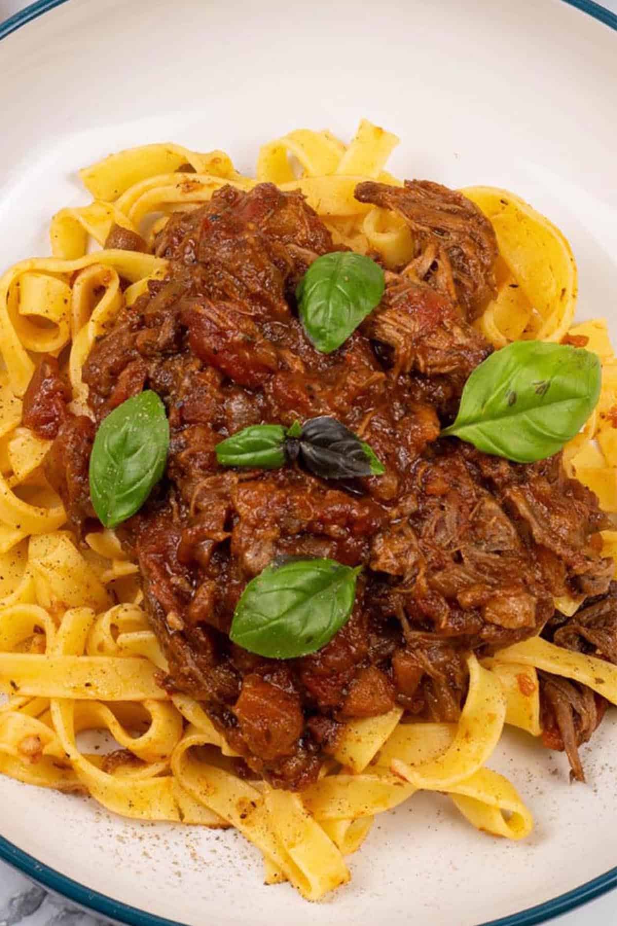 Close up of a portion of slow cooker beef ragu in a pasta bowl with tagliatelle.