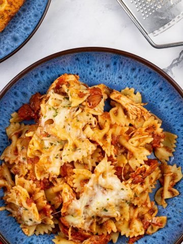 Close up of a portion of slow cooker chicken parmesan pasta in a blue patterned bowl.