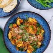 A portion of tortellini with creamy tomato and spinach sauce in a blue patterned bowl with a bowl of green beans and plate of sliced bread on the side.