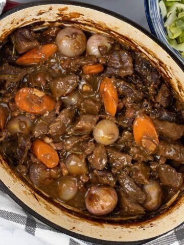 Beef bourguignon in a deep oval casserole dish with a bowl buttered cabbage on the side.