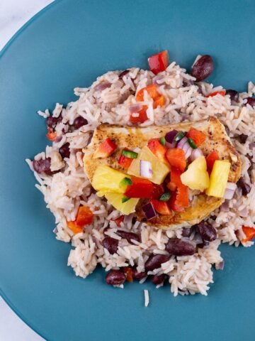 Cajun turkey steak with pineapple salsa and kidney bean rice on a teal plate.