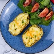 Cheese and spring onion baked potato on a blue patterned dinner plate with salad leaves and tomato wedges on the side.