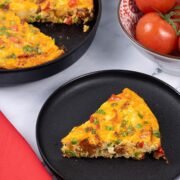 A slice of chorizo frittata on a black side plate with a red napkin on the side.