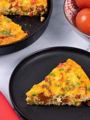 A slice of chorizo frittata on a black side plate with a red napkin on the side.
