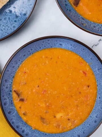Two portions of chorizo and lentil soup in blue patterned bowls with a plate of sliced brown bread on the side.