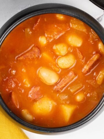 A portion of chunky chorizo and butter bean soup in a black bowl.