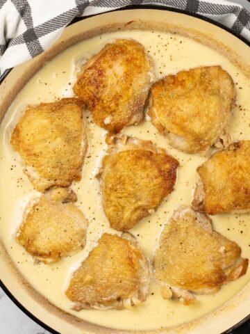 Cider braised chicken thighs in a large round shallow casserole.