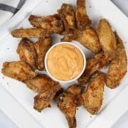 Easy air fryer cajun chicken wings on a white square platter with a dish of cajun dipping sauce.