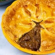 Easy steak pie in a round yellow pie dish with a triangle of pastry cut out.