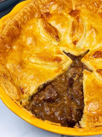 Easy steak pie in a round yellow pie dish with a triangle of pastry cut out.