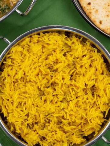 Golden pilau rice in a balti dish with a dish of slow cooker chicken and potato curry, and plate of chapatis in the background.