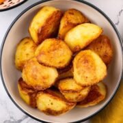 Roast potatoes in a black and cream serving bowl.