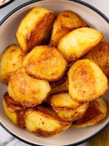 Roast potatoes in a black and cream serving bowl.
