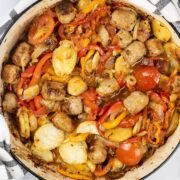 Salsiccia con patate e pomodori al forno in a large round casserole.