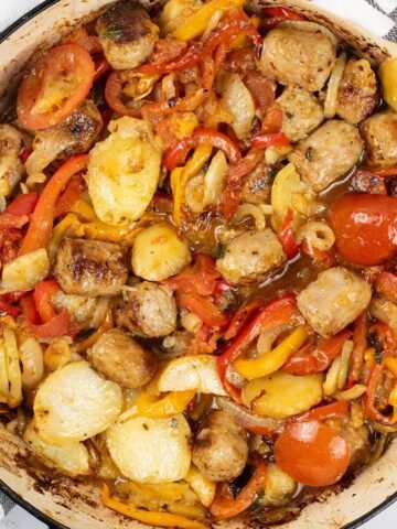 Salsiccia con patate e pomodori al forno in a large round casserole.