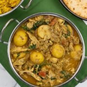 Slow cooker chicken and potato curry in a balti dish with golden pilau rice and chapatis in the background.