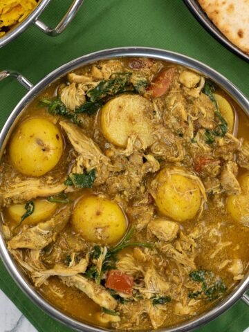 Slow cooker chicken and potato curry in a balti dish with golden pilau rice and chapatis in the background.