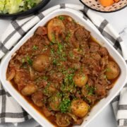 Slow cooker lamb stew with potatoes in a white square serving dish with bowls of buttered cabbage and quick cook carrots in the background.