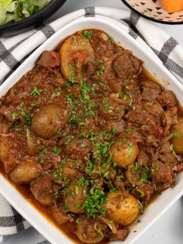 Slow cooker lamb stew with potatoes in a white square serving dish with bowls of buttered cabbage and quick cook carrots in the background.
