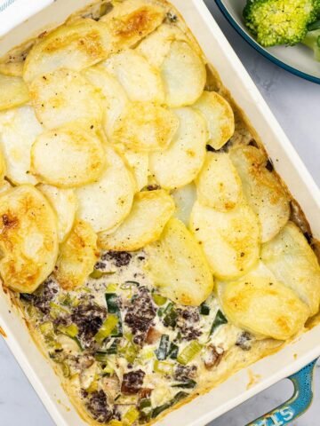 Smoked haddock, black pudding and leek gratin in a rectangle Staub dish with a bowl of broccoli and green beans on the side.