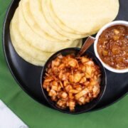 Spicy onions in a black serving bowl sitting on a black dinner plate with poppadoms and a dish of mango chutney.