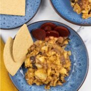 Two portions of stovies in blue patterned bowls, garnished with sliced beetroot and oatcakes.
