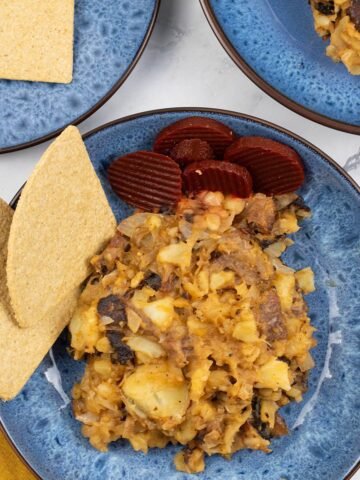 Two portions of stovies in blue patterned bowls, garnished with sliced beetroot and oatcakes.