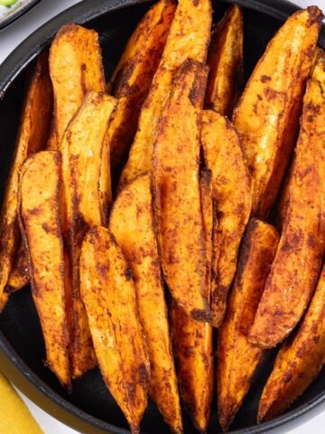 Sweet potato wedges in a black serving bowl with a mustard napkin on the side.
