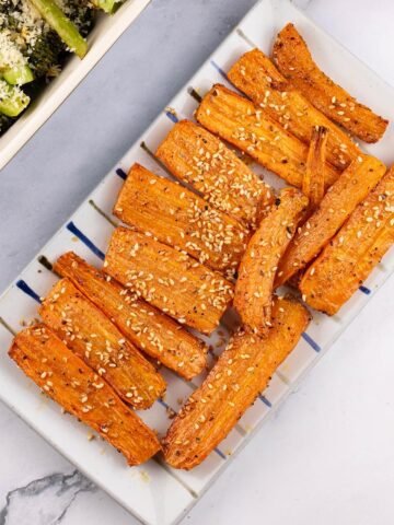 Za'atar roasted carrots on a rectangle striped platter with a dish of tenderstem broccoli on the side.