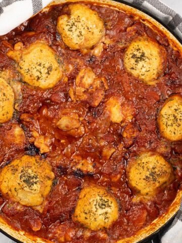 Chicken arrabbiata stew and parmesan dumplings in a shallow round casserole dish.